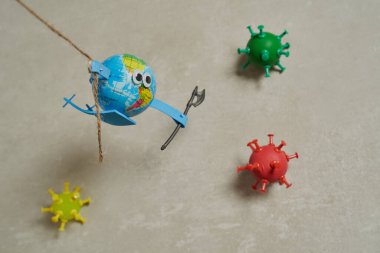 Conceptual photo of an earth toy jumping with a string to fight against three viruses with an ax in the left hand on a grey background. clipart