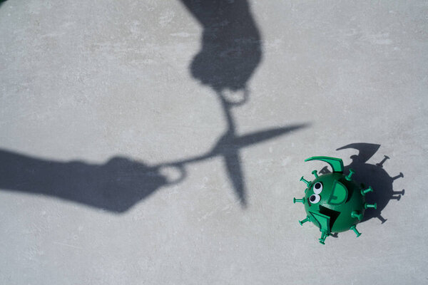 Концептуальное воздушное фото тени ножниц, разрезающих игрушечный зеленый вирус на сером фоне
.