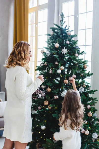 Une fille avec sa mère décorer le sapin de Noël, l'intérieur est décoré pour la nouvelle année et Noël, famille et joie, traditions . — Photo