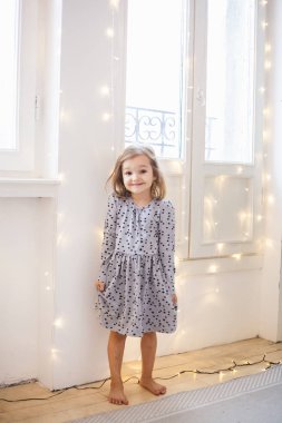 Kız tatil için bir çelenkle süslenmiş pencerenin yanında oturuyor, oda yeni yıl ve Noel için dekore edilmiş.