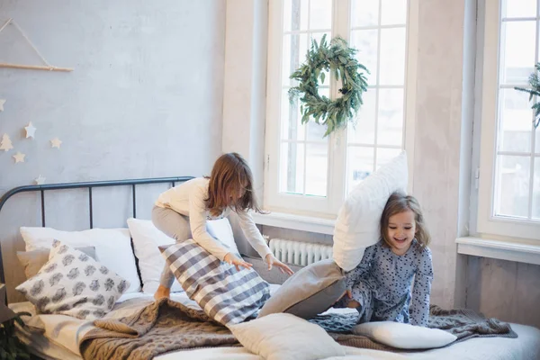Две девочки, сестры дерутся подушки на кровати, окно украшено рождественским венком, жизнь, детство — стоковое фото