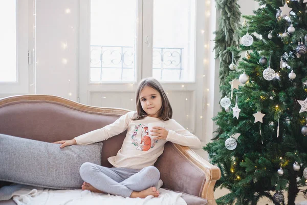 La fille est assise sur le canapé en attendant les vacances, la chambre est décorée pour la nouvelle année et Noël — Photo