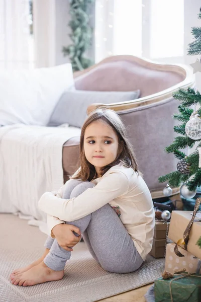 La fille est assise près du canapé et décoré arbre de Noël, la chambre est décorée pour la nouvelle année et Noël — Photo