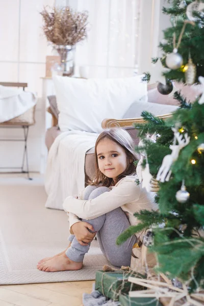 La fille est assise près du canapé et décoré arbre de Noël, la chambre est décorée pour la nouvelle année et Noël — Photo