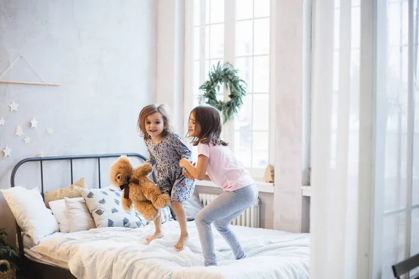 침대에 베개를 놓고 싸우는 두 소녀, 크리스마스 화환으로 장식된 창문, 인생, 어린 시절 — 스톡 사진