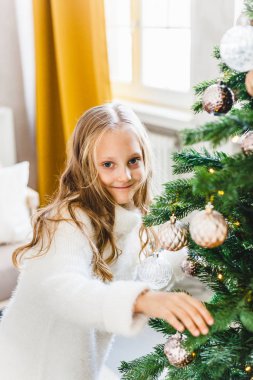 Bir kız süslenmiş bir Noel ağacının yanında duruyor, yeni yıla ve Noel 'e hazırlanıyor.