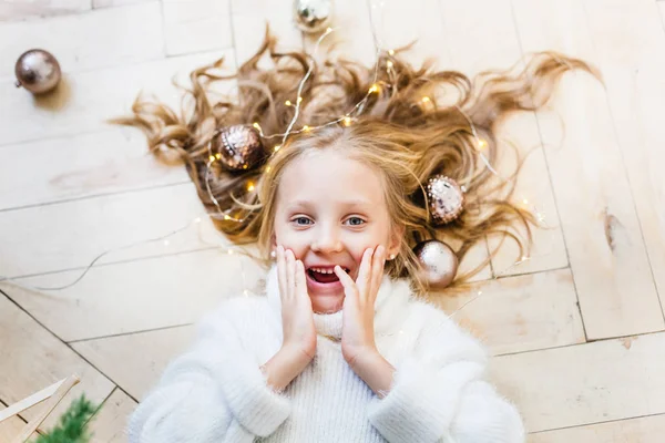 Fille couchée sur le sol, boules dans les cheveux, arbre de Noël et intérieur — Photo