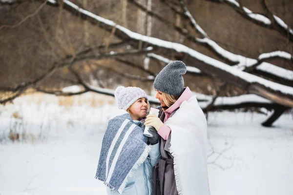 Mother and daughter are walking in the winter forest, wrapped in a blanket, tea or a drink from a thermos — 스톡 사진