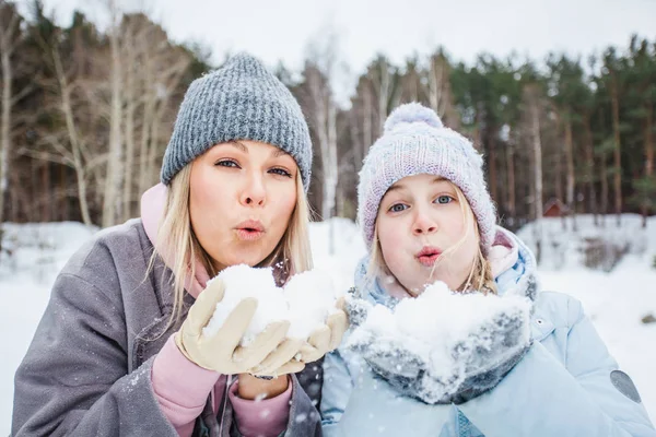 mom and daughter playing with snow, blowing snow from their palms, winter walk