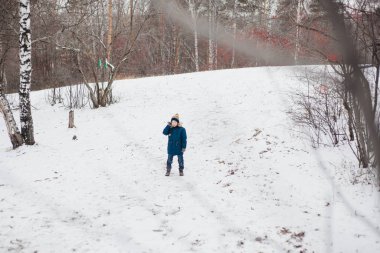 Bir çocuk kış ormanlarında ya da parkta yürür, kalın giysiler kar ve kış sporları.