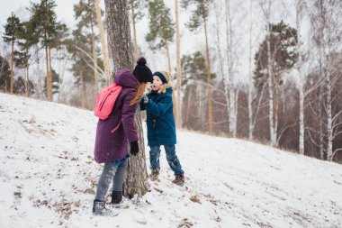 Kız, erkek kardeşiyle bir ağacın yanında durur, ormanda kış yürüyüşü yapar ya da Park 'ta.