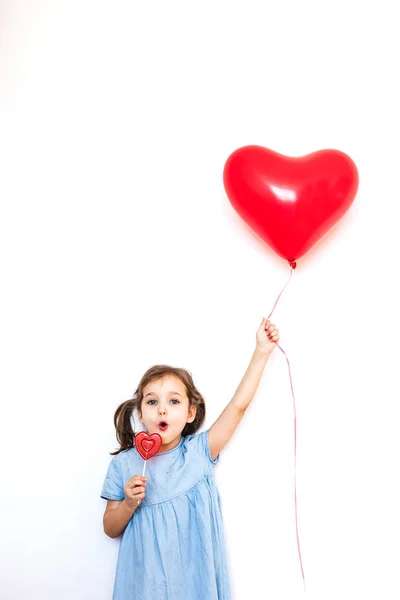 A little girl holding a beautiful red heart-shaped balloon for a Valentine's day gift and a Lollipop in the shape of a heart, lovers, Valentine's day, family and heart — Stock Photo, Image