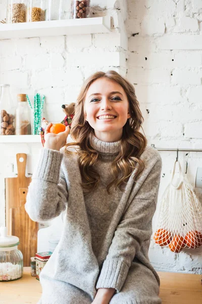 A girl of European appearance is sitting in the kitchen, throwing or holding citrus, tangerine, fun and fun, home and cooking — 스톡 사진