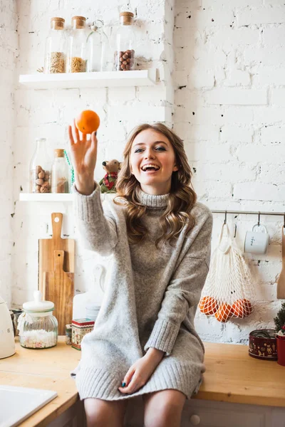 A girl of European appearance is sitting in the kitchen, throwing or holding citrus, tangerine, fun and fun, home and cooking — 스톡 사진