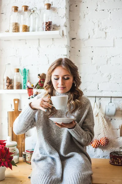 European-looking girl sitting in the kitchen, drinking tea or coffee from a white mug, drink, morning in the kitchen, student, Manager, freelancer — 스톡 사진