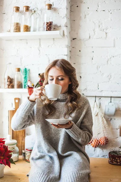 European-looking girl sitting in the kitchen, drinking tea or coffee from a white mug, drink, morning in the kitchen, student, Manager, freelancer — 스톡 사진