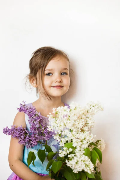 Mała dziewczynka na białym tle stoi i trzyma gałęzie lilii, kwitnący kurst, liliowy, wiosna i lato — Zdjęcie stockowe