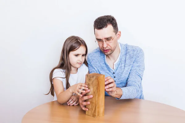 Girl and dad play a game at home, cost a tower of blocks, cubes, jenga, puzzle for brain development, mental intelligence, child development, school, home, quarantine, vacation, time with family