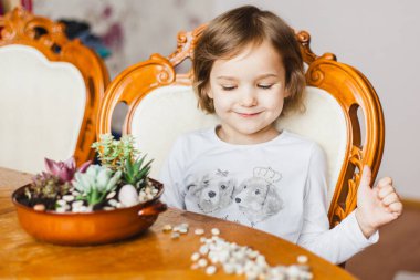 Masada oturan küçük bir kız, bitkiler, sulu saksılar, kaktüsler, içine bitki, ev ve ofis dekorasyonu ve peyzaj, evdeki tropikal alanlar.