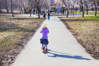 Şapka ve ceket giyen bir kız scooter sürüyor, eğlence ve hareket, diğer çocuklarla iletişim, fiziksel aktivite, oyun