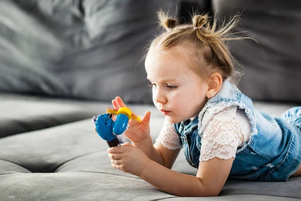 A little girl is sitting on the sofa playing educational games, colored rings, a toy made of wood, family, the development of a child at a young age, tactile sensations
