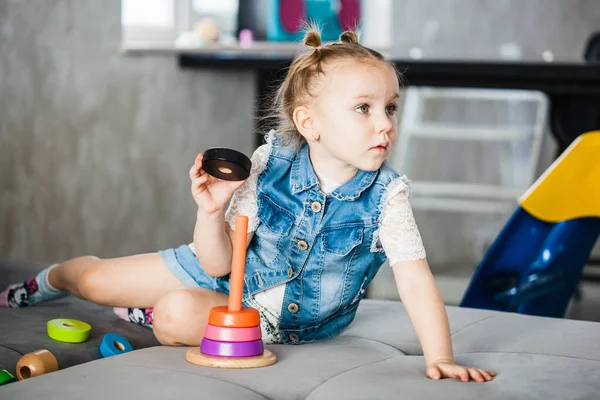 A little girl is sitting on the sofa playing educational games, colored rings, a toy made of wood, family, the development of a child at a young age, tactile sensations