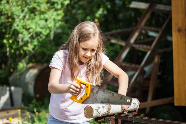 A girl with long hair helps parents in the summer, saws a log with a saw, wood, construction, firewood, stove, game, training