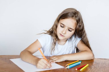 Kız bir defter çiziyor, mektuplar yazıyor, renkli kalemler, evde dersler, çevrimiçi eğitim, zihinsel zeka gelişimi.
