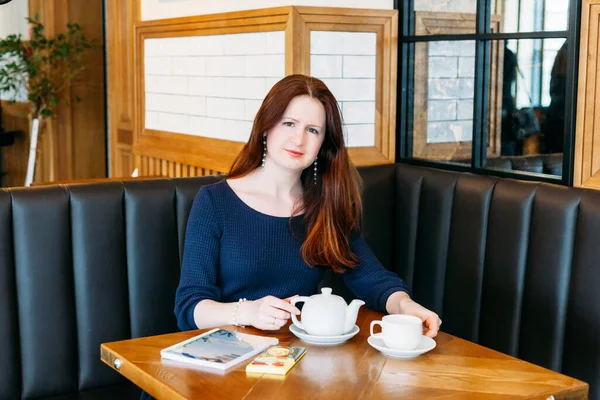 A girl of European appearance in a cafe, drinking tea or coffee from a mug, conversation, meeting, lunch, waiting for a friend