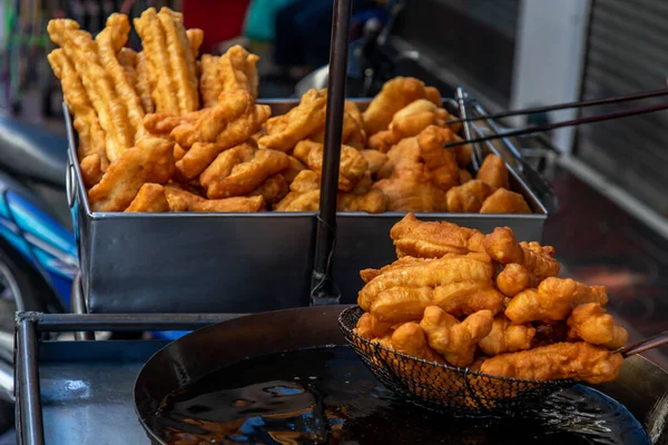 Chinese deep fried dough in hot oil on steel pan. Youtiao, Padnoongo or fried flour sticks is one of the popular breakfasts of Chinese pople, popular street food. Chinese style fried donut.