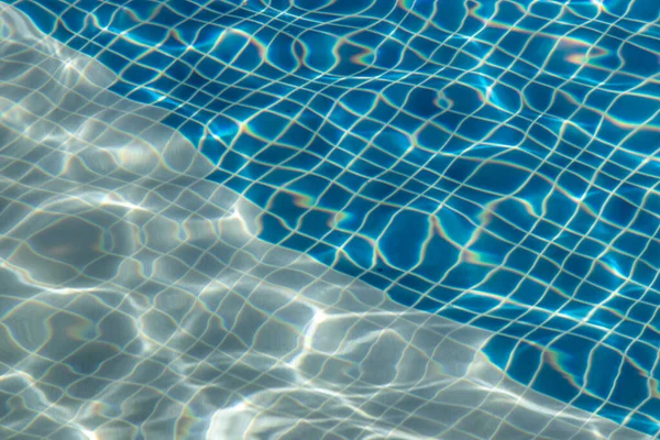 Sun reflection on the blue clear water ripples of swimming pool with mosaic bottom from above. Blue and bright water surface. Copy space, No focus, specifically