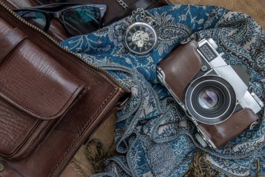 Eski bir fotoğraf makinesi ve kahverengi deri bir çanta eşarp, gözlük ve kese kağıdına takılmış cep saati. Tatil gezisi konsept tasarımı. Klasik renk tonu.