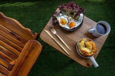 Ispanaklı brioche ile kahvaltı, iki sahanda yumurta, balkondaki ahşap masada sade kahveyle servis edilen meşe yaprağı marulu. Seçici odak.