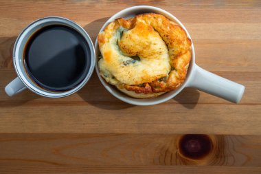 Balkondaki ahşap masada sade kahve ve ıspanaklı brioche ile kahvaltı. Seçici odak.