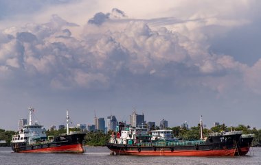 Bangkok, Tayland - 19 Nisan 2020: Chao Phraya Nehri 'nin ortasına park edilmiş iki kargo gemisi ve dramatik gökyüzü geçmişi.