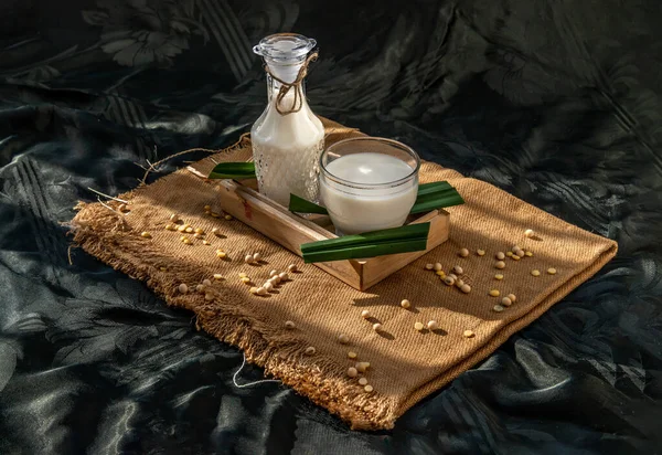 Soy products : A glass of Homemade soy milk and grains (soybeans) in wooden tray and honey with lighting in the morning. Alternative milk concept, Selective focus, Copy space.