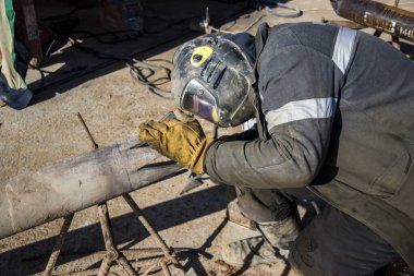 Kaynak yapmak için koruyucu giysili kaynakçı. Sondaj kulesi için boru hazırlığı. İnşaat alanında..