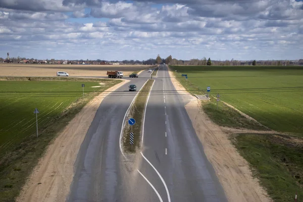 A long two-lane road into the distance. Against the backdrop of a bright cloudy sky.