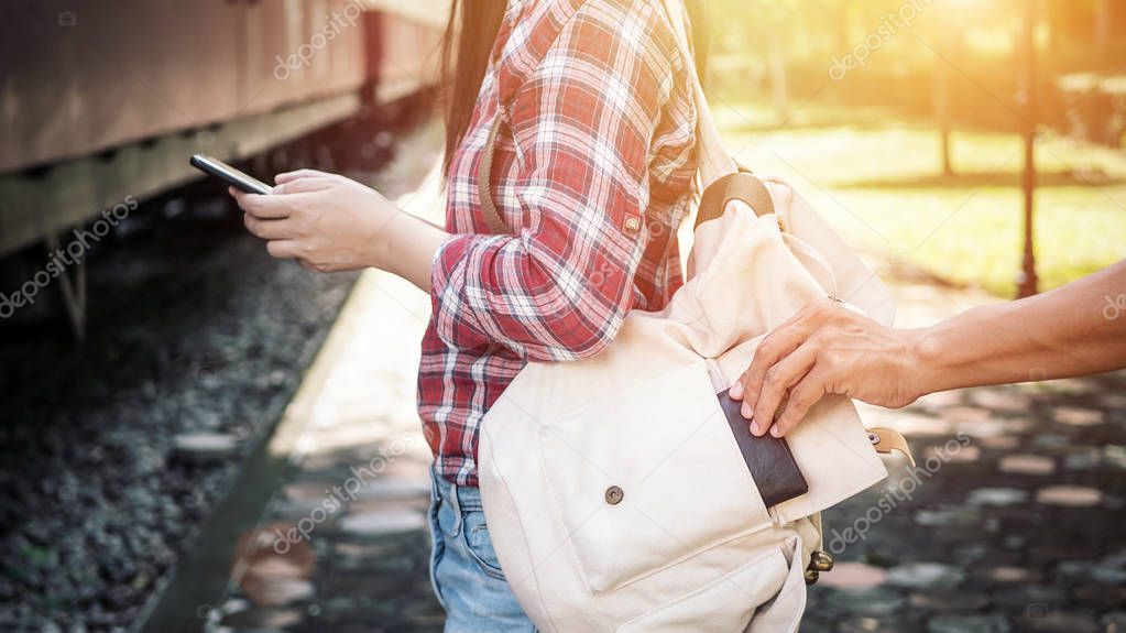 the tourist who were playing mobile phones, she is being tickled by a thief to steal her wallet at the train station. be careful for property safety while traveling concept