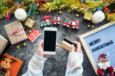 Noel sezonu ve hediye festivali için online alışveriş. Boş ekranlı cep telefonu ve online alışveriş için kredi kartı. Masada Noel süsü olan süslemeler.