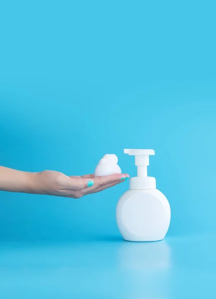 Plastikowa butelka z pompą i pianka musująca lub pianka oczyszczająca na ręce kobiety odizolowane na niebieskim tle, pionowe z przestrzenią do kopiowania. koncepcja czyszczenia — Zdjęcie stockowe