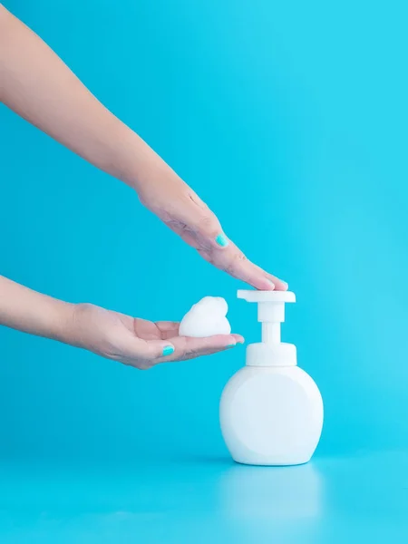 Plastikowa butelka z pompą i pianka musująca lub pianka oczyszczająca na ręce kobiety odizolowane na niebieskim tle, pionowe z przestrzenią do kopiowania. koncepcja czyszczenia — Zdjęcie stockowe