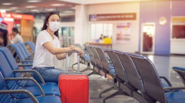 Bagajlı Asyalı turist, Coronavirus 2019 (Covid-19) enfeksiyon salgınından korunmak için havaalanı terminaline giderken hijyenik maske takıyor.