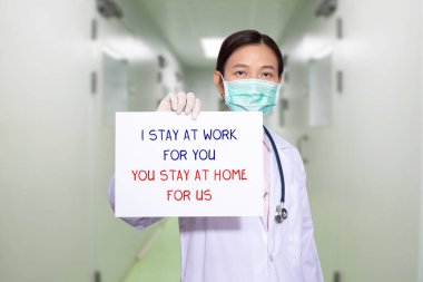 Hastanedeki Asyalı doktor tıbbi maske takıyor, elinde senin için çalıştığım mesajla kâğıt tutuyor, sen de bizim için evde kalıyorsun. COVID-19 Coronavirüs salgınını kontrol altına almak için ev politikası kampanyasında kalın