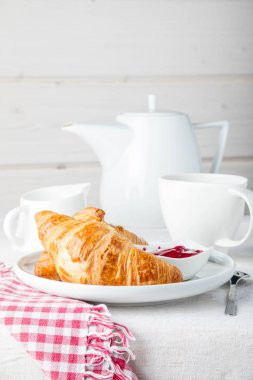 Kahvaltınız kahve, kruvasan ve reçel beyaz masada.