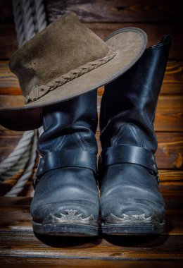 Kovboy şapkası, botlar ve tahta arka planda ip.