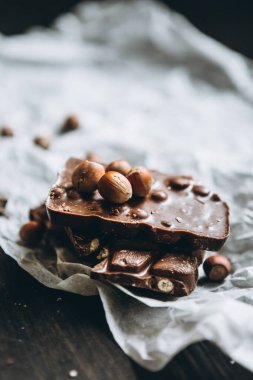 Fıstıklı sütlü çikolata: Fıstık, beyaz parşömen kağıdında fındık ve siyah tahta bir masa. Yakın plan.