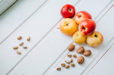 Vitamin patlaması. Sağlıklı meyveler. Doğal vitaminler: kırmızı ve sarı elma, şam fıstığı ve beyaz ahşap arka planda ceviz. Avitaminoz. Süpermarketteki meyveler. Vitamin kutusu