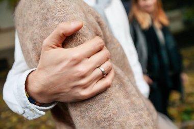 Bir erkeğin eli, bir kızı omzunun üzerinden kucaklar. İki kişilik aşk hikayesi. Adam sonbaharda sokakta bir kıza sarılıyor.