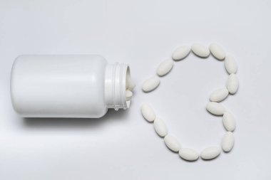 Kalp şeklinde beyaz yuvarlak tabletler beyaz bir kavanozda yatar ve etrafa saçılırlar.